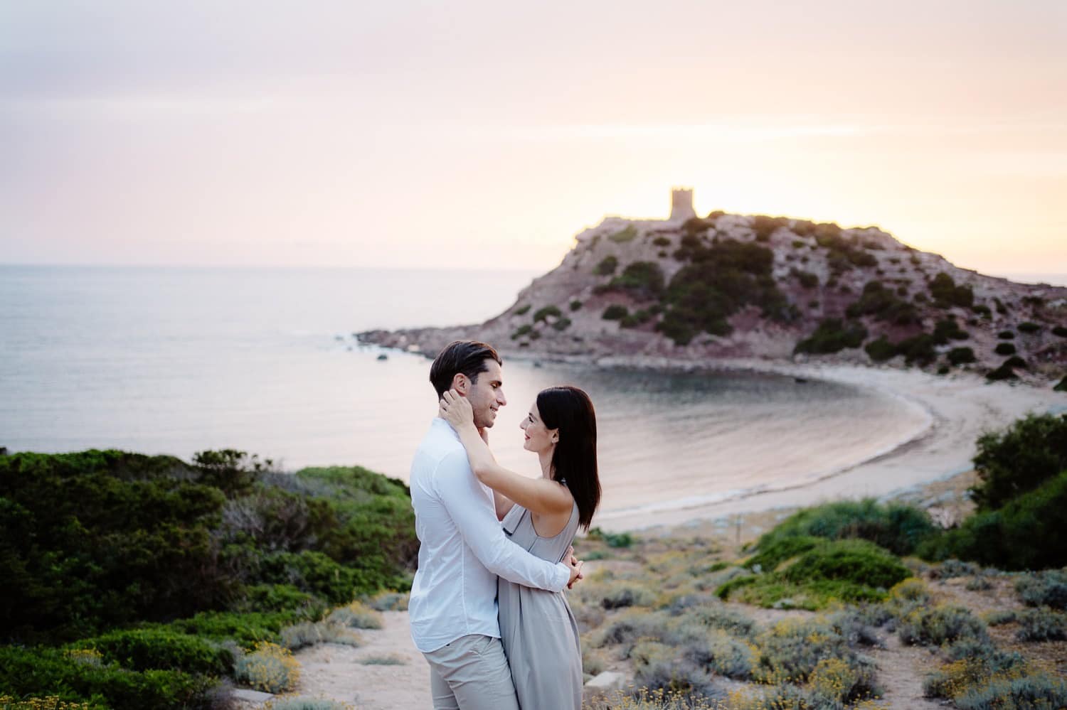 Couple sitting on a rock in front of the sea during their engagement in Alghero.