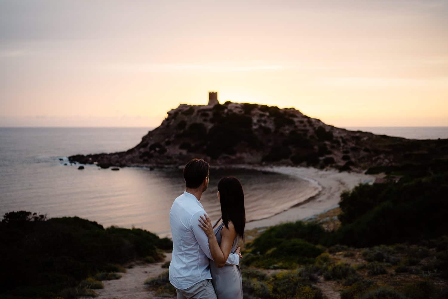 Couple embracing and kissing on a cliff overlooking the sea during their engagement in Alghero.