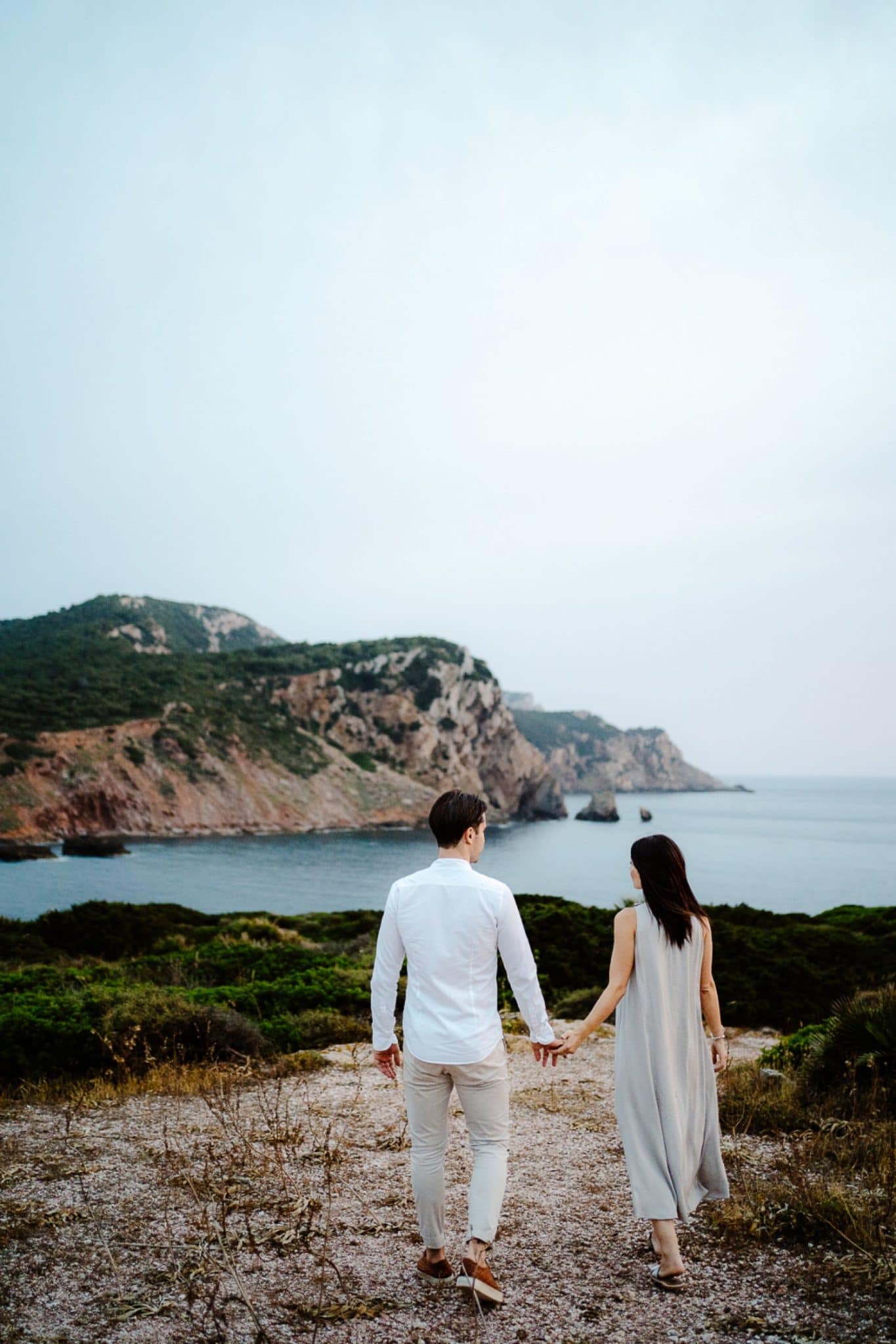 Couple standing on a rocky cliff overlooking the sea in Alghero, photographed by Valeria Mameli