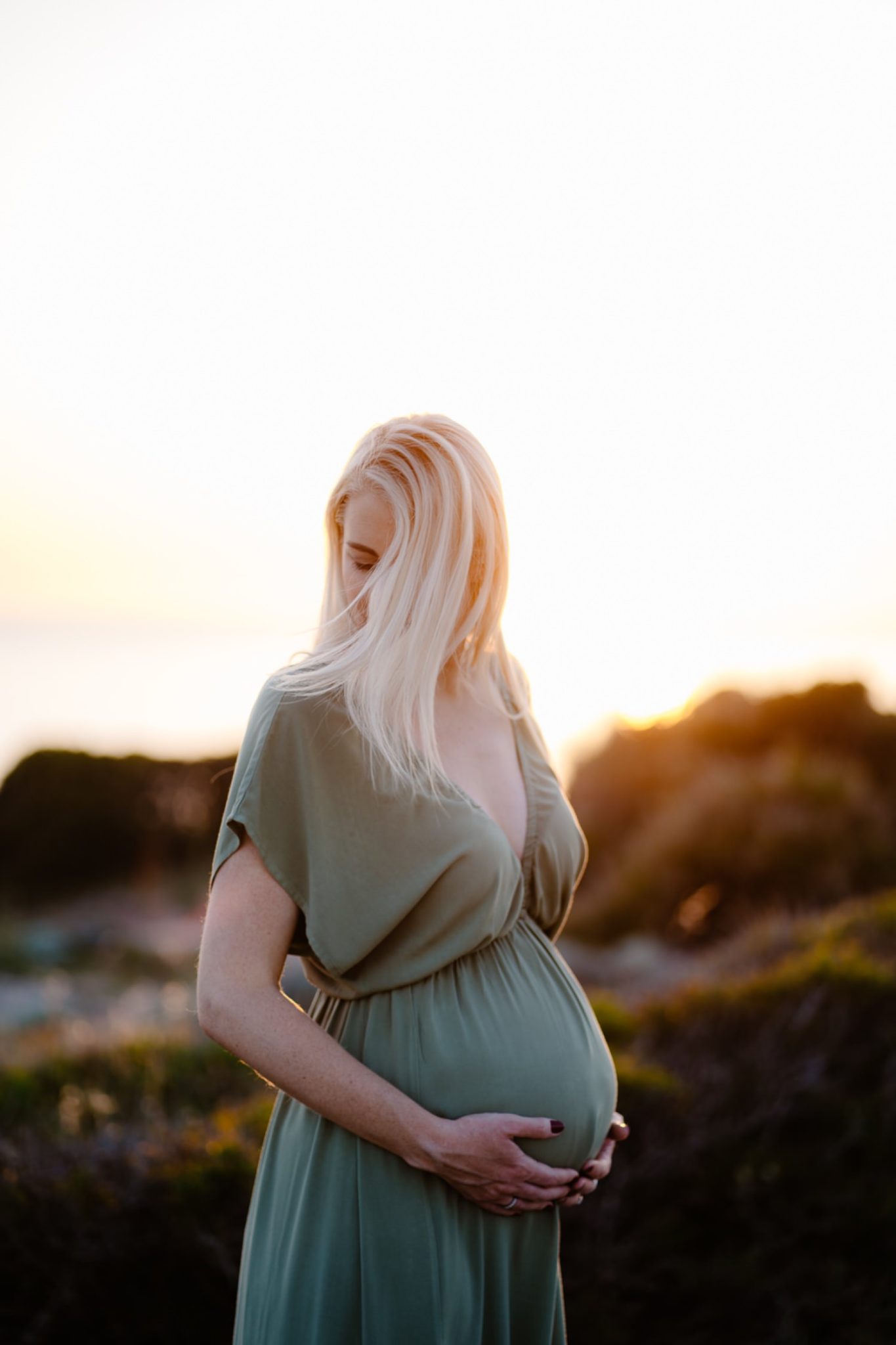 A stunning maternity photo taken in the beautiful coastal town of Alghero. The mother-to-be stands on a rocky beach with her flowing white dress blending in perfectly with the waves crashing behind her.