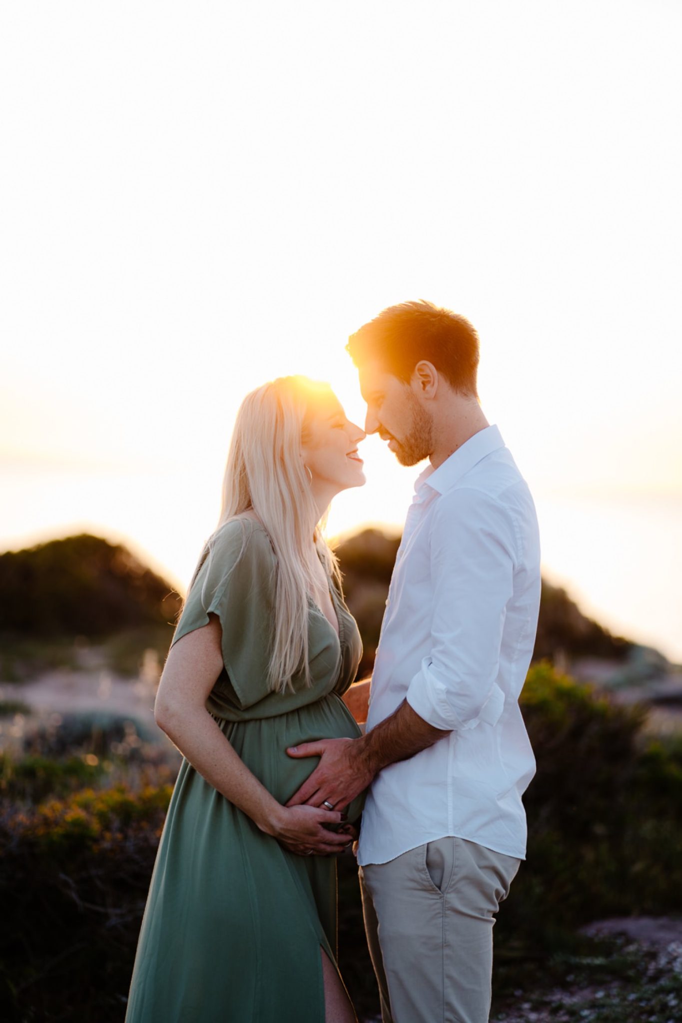 A stunning maternity photo taken on a rocky beach in Alghero. The mother-to-be is standing in the water, with her dress flowing in the wind, and the golden sunset creating a breathtaking background.
